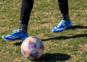 A person in blue and black soccer shoes kicking a soccer ball